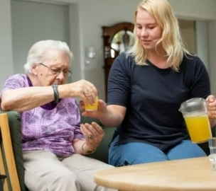 Social- og sundhedshjælper skænker juice til ældre kvinde